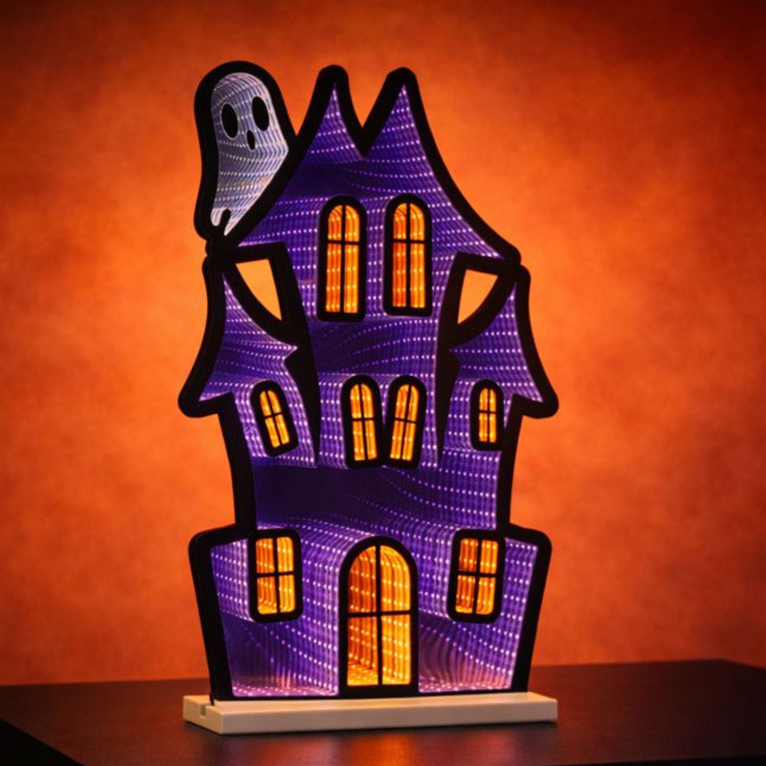 Glowing haunted house and ghost decoration against a rich orange backdrop